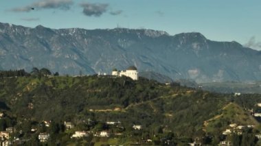 Los Angeles 'taki yeşil parkın üzerinde uçan bir helikopter. Sinematik Kaliforniya tarihi Griffith gözlem evi ve yeşil tepelere park dağ zirveleri ve hareketli arka planda mavi gökyüzü