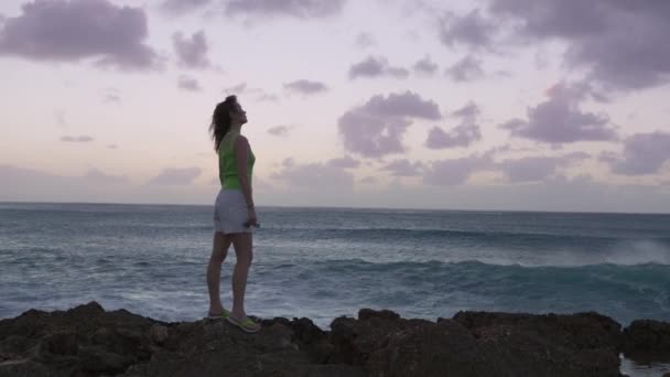 黄昏时分 人物形象的女人举起胳膊 在空中观察海浪冲撞岩石和喷射 感情用事 生活幸福的概念 夏威夷环球旅行慢速4K — 图库视频影像