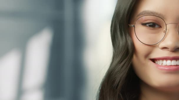 現代の眼鏡で素晴らしいアジアの若い女性の目 美しい顔かなり中国の女の子屋内でぼやけた灰色のニュートラルな背景にポーズ 民族概念クローズアップ肖像画 本物の人々 4Kショット — ストック動画