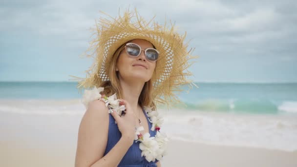 夏休みにビーチを歩いている間に笑顔Bohoスタイルの紫のドレスで美しい若い女性の肖像画 幸せな女性身に着けている花レイと空想のわら帽子 ハワイ島クルージング オアフ島4K — ストック動画