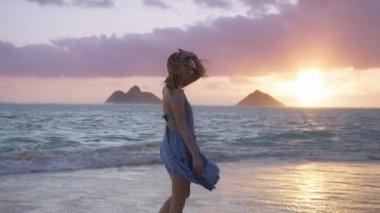 Güzel, el sallayan bir elbise giymiş bir kadın sinemada pembe gün doğumunda. Ağır çekim kadın manzaralı plaj manzarasının keyfini çıkarıyor. REC kamera 4K. Oahu Hawaii Adası ABD 'de yaz tatilindeki kadın turist.. 