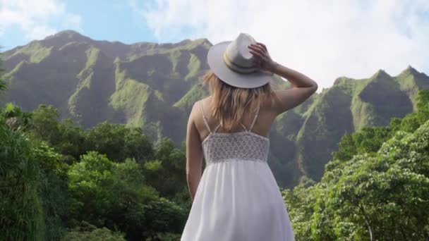 身披白衣 头戴草帽 身披绿色热带丛林 身材苗条的美丽女子 高高地伸展着双臂 感受着自由 幸福的概念 — 图库视频影像