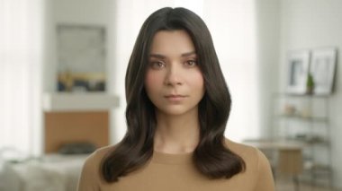 Bej rengi günlük hırkalı, sağlıklı, parlak saç stili olan güzel, melez bir kadının portresi evde kameraya bakıyor. Üzgün, Latin, esmer kızı kapatın.