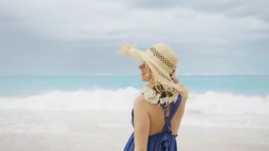 Romantik bir kadın elini kaldırıyor özgür hissediyor, Hawaii sahillerinde dinleniyor arka planda güzel bir deniz mavisi var. Lei Flowers 'ın son moda boho tarzı elbisesinin arkasındaki kız. Yaz tatili, gezi tatili, 4K