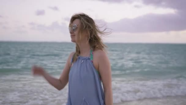 在瓦胡岛海滨 戴着太阳镜的年轻女子脸上挂着微笑 享受着微风 无忧无虑的美国女人 带着柔和的苍白背景 带着大海微笑 美丽的女孩在夏威夷海滩享受早晨 — 图库视频影像