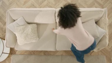 Kıvırcık saçlı neşeli kız evdeki kanepede eğleniyor. Mutlu gençler konsepti. Afro-Amerikalı kadın kazanan koltuğa düşüşünü kutluyor. Tepeden tırnağa coşkulu kadın uzak bir iş fırsatı elde etti.