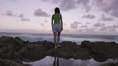 Yeşil bluzlu özgür mutlu genç gezgin kadın okyanusa bakıyor, doğada okyanus esintisinin tadını çıkarıyor temiz hava soluyor, rüzgarda uçuşan saçlar. Rocky Ocean Plajı 'ndaki insanlar. Özgürlük Kavramı, Mutluluk Yolculuğu