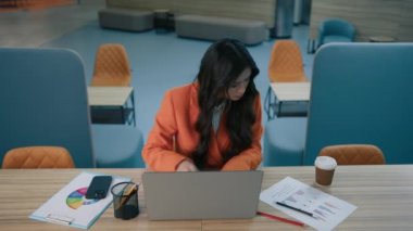 Neşeli Asyalı genç iş kızı internetten iş mesajları yazan, içeride kahve içen online ortaklarla dizüstü bilgisayar ağı kullanıyor. Açık uzay ofisinde çalışan güzel insanlar.