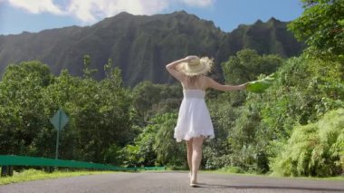 Hawaii, Oahu Adası 'ndaki doğa parkında mini boho beyaz elbise ve büyük hasır şapkalı güzel, şehvetli genç bir kadının yavaş görüntüsü. ABD 'nin egzotik tropik ada seyahatindeki turizmi