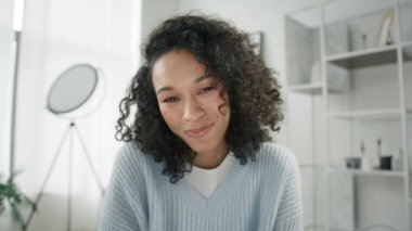 Gülümseyen Afro-Amerikan kadın koç vlog blogu webcam 'de konuşuyor takipçilerine ve hayranlarına hava öpücüğü gönderiyor. Mutlu kıvırcık kız kameraya bakıyor ve uzaktaki arkadaşına video çağrısı yapıyor.