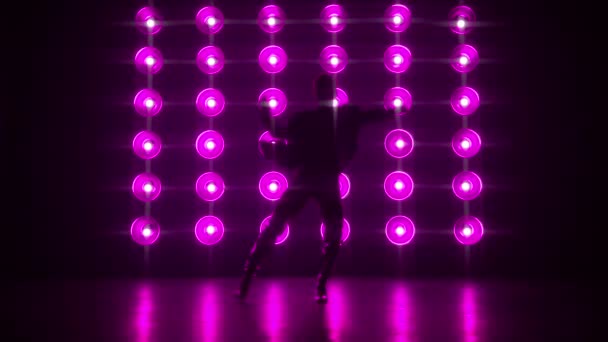 セクシーなポップやモダンなヒップホップダンスを行うスタイリッシュなプロのダンサーのシルエットカラフルな光の壁に電球ランプとプロダクションスタジオ環境でのダンスムーブ暗い神秘的な背景 — ストック動画