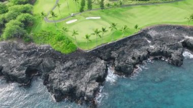 Sinematik siyah lav sahili ve şeffaf mavi okyanus suyu 4K olan yeşil golf sahasının üzerinde güzel bir hava aracı. Büyük Ada tropikal sahili Hawaii ABD 'de mavi okyanus manzarası