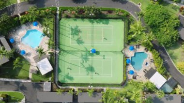 Tenis kortunun yukarısına aktif oyun maçında drone atışı yap. Plaj villaları ya da kulübeleri olan tropikal yeşil otel bahçesindeki tenis kortunun arka planı, Hawaii ABD yaz gezisi 4K