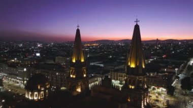 Meksika 'nın Guadalajara şehrinin üzerinde güzel pembe gün batımı gökyüzü. Gece aydınlatmalı tarihi mimari katedralinin insansız hava aracı. Guadalajara Katedrali ve Central Plaza Jalisco. Latin şehri
