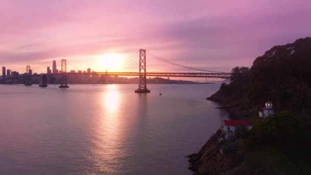 エレバブエナ島の小さな歴史的灯台の建物からの空中の景色は サンフランシスコのダウンタウンの上に黄金の夕日の空を上昇しました 宝島に赤屋根の灯台建物 — ストック動画