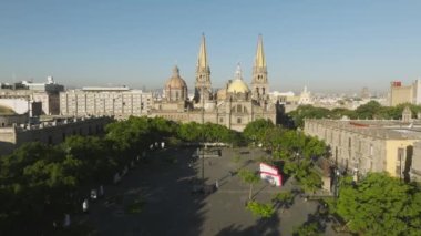 Gökyüzü karenin üzerinde, Gotik kuleleri olan güzel mavi gökyüzü. Guadalajara 'daki yeşil plaza parkı. İHA, Liberacion 4K plazasında yavaş uçuyor. Guadalajara Katedrali cephe manzarası, Latin Meksika