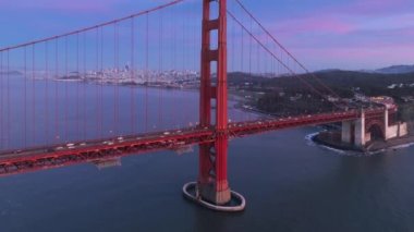 San Francisco sinematik günbatımında bir dönüm noktası. Golden Gate Köprüsü 'nün ve şehrin ufuk çizgisinin hava görüntüsü. Pembe gökyüzü arka planı 4K ABD 'de gece aydınlatma ile kırmızı asma köprü güzel drone görüntüleri