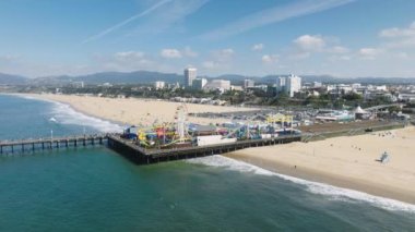 Santa Monica İskelesi, güneşli bir yaz günü, Los Angeles. Okyanus kıyısından tarihi Santa Monica iskelesindeki eğlence parkının hava görüntüleri. Şehrin güzel manzarası, arka planda, kumlu plaj 4K 'de.