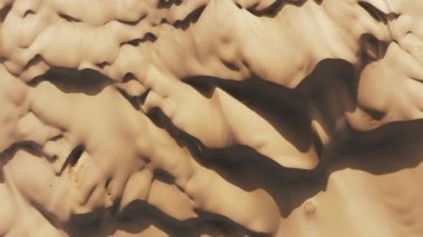 4K yukarıdan aşağı soyut dalgalı desenli bej rengi altın çöl yüzeyi günbatımı ışığı ve yüksek kum tepelerinin derin gölgeleri ile boyanmış. Vahşi çöl doğasının hava manzarası.
