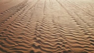 Dalgalı yüzeyi güçlü rüzgarla savrulan altın kumun üzerinde uçan dron. Derin gölgeli kum tepesi dokusu. Gün batımında hava manzaralı çöl doğası 4K. Güzel Sahra Çölü manzarası