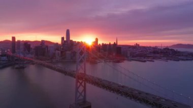 Finans bölgesi binaları ve Bay Köprüsü 'nün üzerinde gün batımı gökyüzü. San Francisco şehir merkezinde, destansı mor günbatımı gökyüzü 4K hava sahasında. San Francisco üzerinde dramatik pembe gün batımı bulutları
