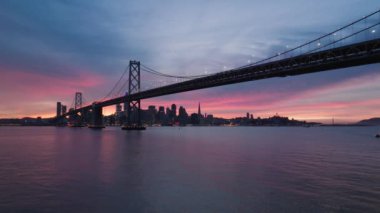 San Francisco 'nun klasik panoramik manzarası ünlü Oakland Bay Köprüsü yazın dramatik günbatımında güzel pembe akşam ışığı ile aydınlatılıyor. San Francisco Körfezi California ABD Hava 4K