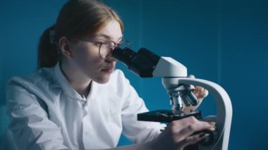 Bilim adamı mikroskop altında arıyor. Güzel beyaz kadın portresi tıbbi gelişim laboratuarında petri kabı örneğini analiz ediyor. Bilim insanları tıbbi laboratuvarda biyoteknoloji araştırması yapıyor.