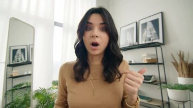 Genç İspanyol, zoom görüntülü konuşma sırasında fırça çekti. Latin bir kadın video konferans görüşmesinde kameraya çekmek için birine parmağını sallıyor. Şüpheci genç İspanyol kadın ev masası 4K 'da kameraya konuşuyor.