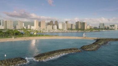 Waikiki plajı altın günbatımı saatinde binalara yerleşir ve mavi okyanus yüzeyi ABD 4K 'ya ışık yansıtır. Honolulu şehir manzarası, Waikiki 'nin gökyüzü manzarası. Sihirli ada sahil parkında Ala Wai tekne limanı