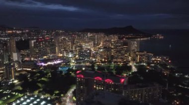 Honolulu şehir merkezindeki Waikiki plaj tatil köyü gökdelenleri ve otel binalarının hava manzarası. Karanlık yaz gece ışığı. 4K B-roll İHA çekim sahnesi. Oahu Hawaii Adası 'ndaki aydınlatılmış gece şehri ABD