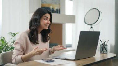 Gülümseyen İspanyol bayan öğretmen çevrimiçi öğretmen olarak çalışıyor, öğrencilerle konferans görüşmesi yapıyor. Görüntülü sohbetteki genç kadın ofis masasında İspanyolca öğretirken dizüstü bilgisayar kamerasına bakıyor.