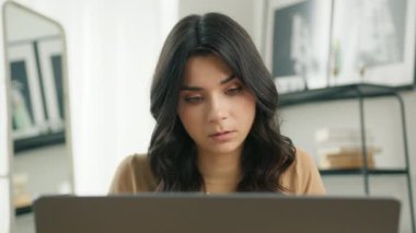 Bin yıllık ciddi İspanyol kökenli serbest öğrenci ev ofisinde oturan dizüstü bilgisayarı kullanarak serbest çalışıyor. 4K apartmanında uzaktan not defterine yazan odaklanmış karışık ırk girişimcisi
