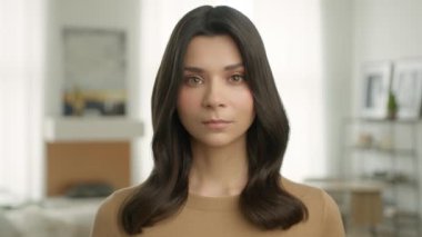 Bej rengi günlük hırkalı, sağlıklı, parlak saçlı, ciddi, genç, melez bir kadının portresi evde kameraya bakıyor. Üzgün Latin esmer kız 4K 'yi kapatın.