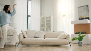 Evde dans eden neşeli, genç bir kadının Yavaş Hareketi. Çoklu etnik kökenli İspanyol kız komik dans hareketleriyle kutluyor, haftasonu özgürlüğün tadını çıkarıyor, 4K çekim tarzı oturma odası.