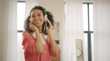 Mutlu Afro-Amerikan kadın kulaklık takıyor evde tek başına dans ediyor. Gülümseyen genç melez bayan hipster modern çatı katında müzik dinliyor, kendini özgür ve eğlenceli hissediyor.