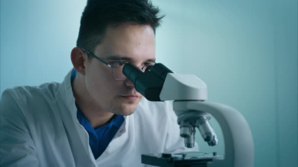 医学研究者の肖像男性は顕微鏡を用いた健康診断実験を行い 生物学研究室の試料を分析する プログレッシブサイエンス研究所でエンジニアを統一 — ストック動画