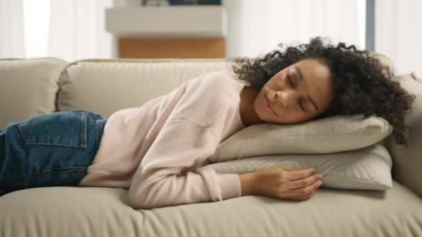 若い疲れ混合レースフリーランスの女性が自宅で快適なソファの上で寝ています アフリカ系アメリカ人の少女は目を閉じてソファの枕の上に寝そべっていた ソファで夢を見て 夜不眠症のコンセプト — ストック動画