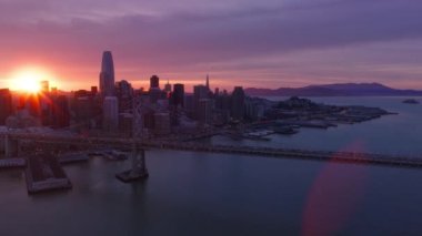 San Francisco şehrinin altın saatinde, gün batımında gül sarısı bulutlarla kayan hava çekimi. Yanan kızıl güneş bir taraftan diğer tarafa 4K ABD 'ye geçiyor. Şehir merkezindeki gökdelenler silueti