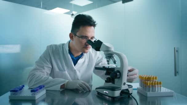 在显微镜下观察疲倦的科学家男性的画像 分析培养皿样品 做药物的大制药实验室在医学发展实验室工作的聪明人的概念 — 图库视频影像