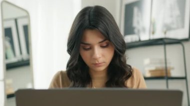 Ev ofisinde dizüstü bilgisayar kullanan konsantre olmuş Latin kız öğrenci portresi. 4K Slowmo apartmanında uzaktan not defterine yazan odaklanmış karışık ırk girişimcisi