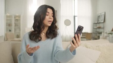 Modern teknoloji kavramı, aile yavaş çekim 4K video ile kablosuz bağlantı. Kocasıyla, erkek arkadaşıyla ya da akrabalarıyla kanepesinde selfie ya da video görüşmesi yapan otantik, mutlu, zarif bir kadın.
