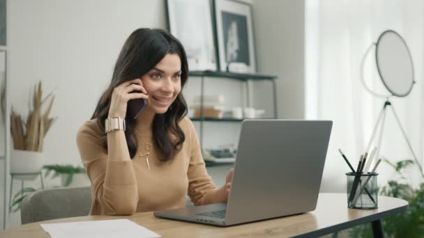 Laptop Kullanarak Telefonla Konuşan Gülümseyen Genç Spanyol Kadını Ofis Masasında — Stok video