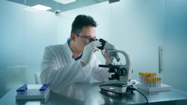 医学研究者の男は 科学研究所のデジタル顕微鏡下で生物学的サンプルを見て ワクチンや医薬品に取り組む白衣のスマート白人男性研究室エンジニア — ストック動画