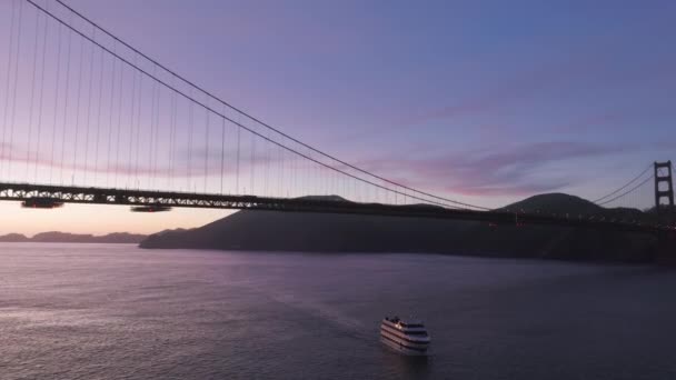 サンフランシスコ湾の象徴的なゴールデンゲートブリッジの景色を楽しむために航海中の観光客と日没クルーズボートツアーの航空機を閉じます 劇的なピンクの夕日の空での映画観光名所のランドマーク — ストック動画