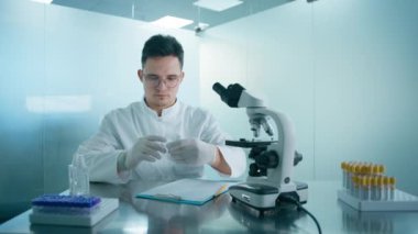 Profesyonel laboratuvar 4K 'de beyaz üniformalı bir mühendis. Test tüpleri ve mikroskop kullanarak tıp araştırmacısı tarafından yürütülen DNA test deneyi ve biyoloji laboratuvarında rapor analizi.