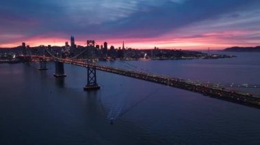 Bay Köprüsü 'nü geçip San Francisco şehir merkezine giden trafiğin insansız hava aracı görüntüsü. San Francisco 'nun gökdelenlerinin siluetleri ve gece aydınlatması uzaklardan görülüyor.