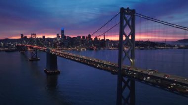 Gece trafiğiyle dolu San Francisco Oakland Bay Köprüsü 'nün havadan görüntüsü. Finansal bölge silueti arka planda dramatik renkli günbatımı gökyüzünde. San Francisco, Kaliforniya 'nın sinematik manzarası