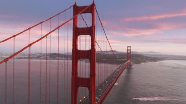 San Francisco 'daki Golden Gate Köprüsü' nü dramatik bir şekilde altın gün batımı ışığında kapatın. Hareket halindeki pembe bulutlu ünlü Golden Gate Köprüsü 'nün sinematik hava manzarası, San Francisco ABD