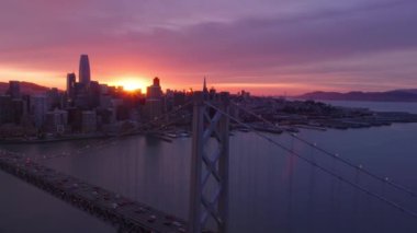 San Francisco şehir merkezinin ve Kaliforniya 'daki Bay Bridge' in havadan manzarası. San Francisco 'nun 4K insansız hava aracı görüntüsü pembe mor bulutlu, pembe gül sarısı günbatımında gökyüzü