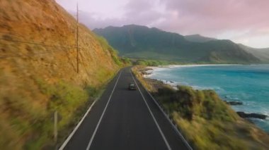 Oahu Adası 'ndan Hawaii ABD' ye seyahat eden turistler. Sinematik sahil şeridi boyunca araba sürüyor. Dramatik kayalık okyanusun üzerindeki hava yolu yeşil volkanik dağlara doğru ilerliyor. Mutlu yaz tatillerinin arka planı